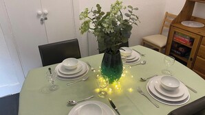 A dining table set with white plates, bowls, and cutlery, a green vase with a plant, and fairy lights. - 3 bedroom accommodation in Comrie, near Crieff (Comrie, near Crieff)