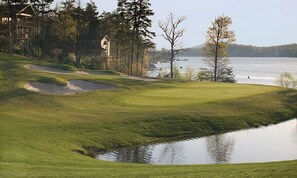 Stunning golf course with well-maintained fairways and sand bunkers, set amidst a tranquil landscape with a picturesque body of water and a resort-style lodge in the background.