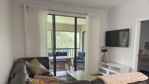 A modern living room with a dark leather sofa, a white coffee table, and a flat-screen TV mounted on the wall. - Remodeled, Luxurious 2BR+2Bath by IMG+Beach (Bradenton)