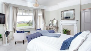 A bedroom with a large bed, a dresser, a mirror, a fireplace, and a view of the outdoors. - 5 bedroom accommodation in Paignton (Paignton)