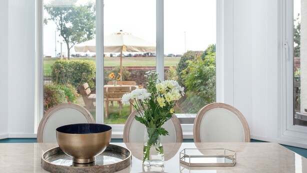 A dining table with a bowl and vase, chairs, and a view of an outdoor area with umbrellas and greenery. - 5 bedroom accommodation in Paignton (Paignton)