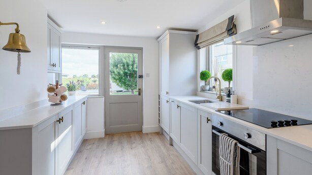 A modern kitchen with white cabinetry, a stainless steel oven, and a window with a view of greenery.