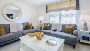 A modern living room with a grey sofa, a white coffee table, and a round mirror on the wall.