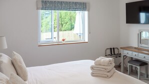 Un dormitorio con cama, escritorio, silla, televisor y ventana con vistas a zonas verdes.