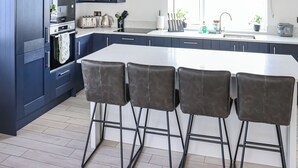 Una cocina moderna con armarios azul oscuro, una isla central con taburetes de bar, horno empotrado y ventana con vistas.