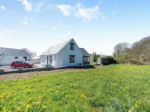 A white house with a sloped roof, a driveway, and a field of yellow flowers in the foreground. - Preselli View Cottage - UK37755 (Ludchurch, near Narberth)