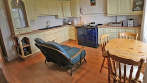 A kitchen with wooden cabinets, a stove, a dining table, and two chairs. - 2 bedroom accommodation in Kilmaluig, Isle of Skye (Kilmaluig, Isle of Skye)