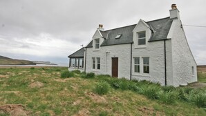 A white house with a dark roof, a chimney, and a door. - 2 bedroom accommodation in Kilmaluig, Isle of Skye (Kilmaluig, Isle of Skye)