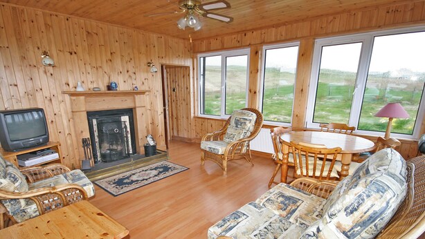 A wooden interior with a fireplace, television, wicker furniture, and large windows. - 2 bedroom accommodation in Kilmaluig, Isle of Skye (Kilmaluig, Isle of Skye)