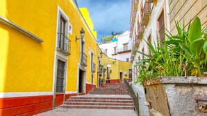 A narrow street with yellow buildings, a staircase, and a metal railing.
