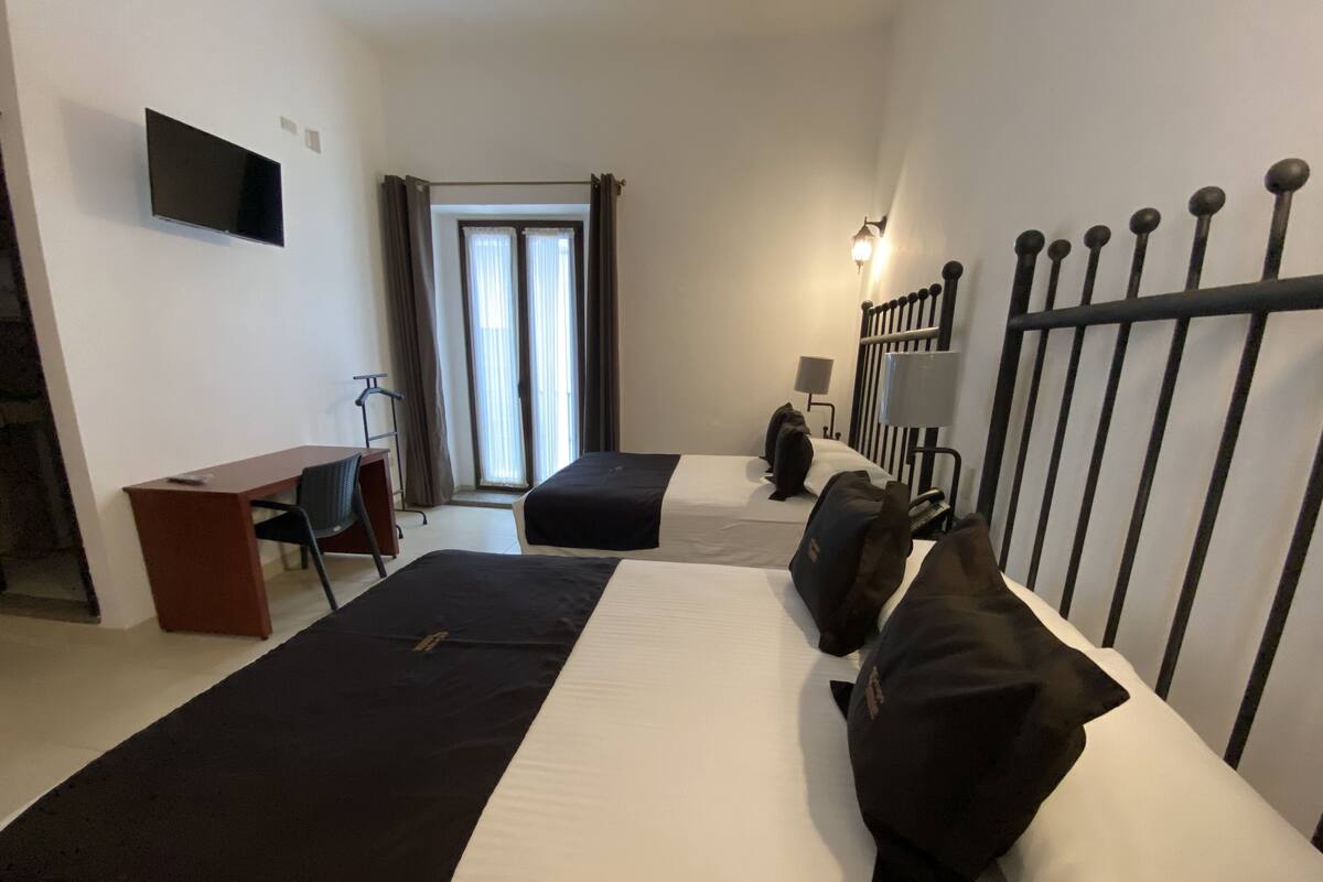 Hotellihuone, jossa on kaksi sänkyä, työpöytä, tuoli, televisio ja ikkuna, jossa on verhot.