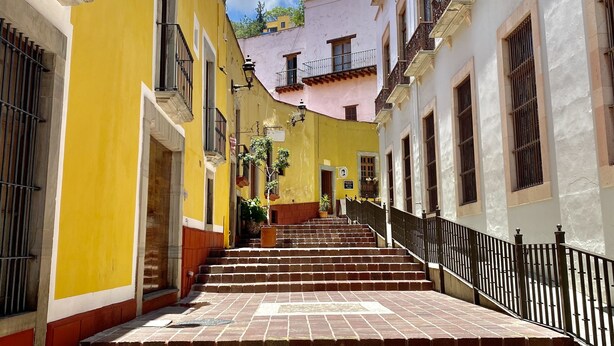 A narrow street with steps leading up to a building with balconies and a yellow facade.