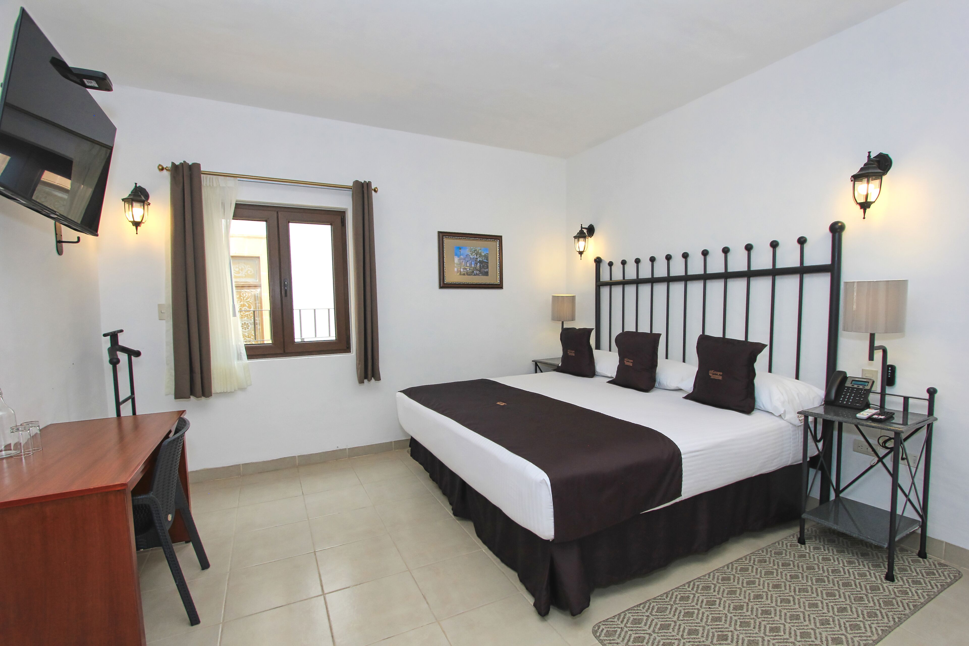 A hotel room with a bed, bedside tables, a desk, and a TV.