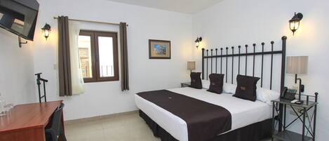 A hotel room with a bed, bedside tables, a desk, and a TV.