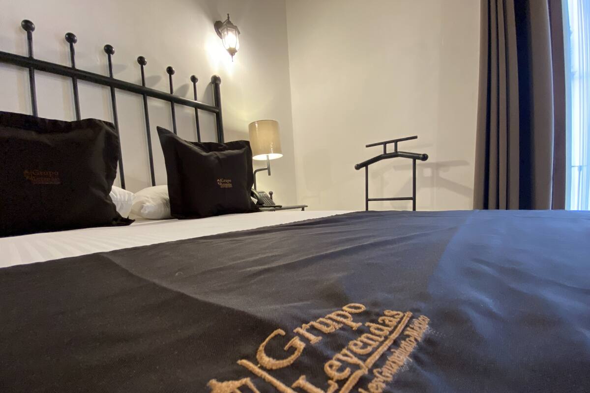 Siisti hotellihuone, jossa on huolitellusti pedattu sänky, musta pääty, yöpöytälamppu ja ikkuna, jossa on verhot.