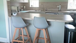 Une cuisine avec un plan de travail en bois, deux tabourets de bar, un évier, une fenêtre et un lave-vaisselle.