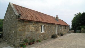 Un bâtiment en pierre avec un toit recouvert de tuiles rouges, une petite fenêtre et des plantes en pot disposées le long de la façade.
