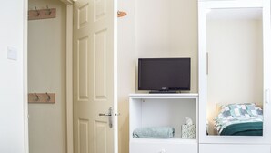 Ein Schlafzimmer mit einem Bett, einem Fernseher auf einem Regal, einer Tür und einer weißen Kommode.