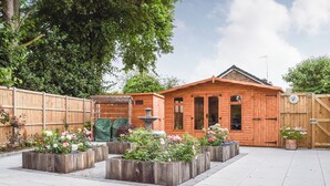 Eine Holzhütte mit einer gefliesten Terrasse, umgeben von einem Holzzaun und verschiedenen Blumentöpfen.