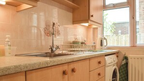 Eine Küche mit Spüle, Arbeitsplatte, Holzschränken, einer Waschmaschine und einem Fenster mit Jalousien.