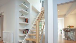 Un intérieur moderne avec un escalier en bois, des étagères blanches et un coin cuisine.