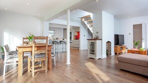 Un vaste espace de vie comprenant une table à manger en bois, un canapé et une cuisine à l’arrière-plan.