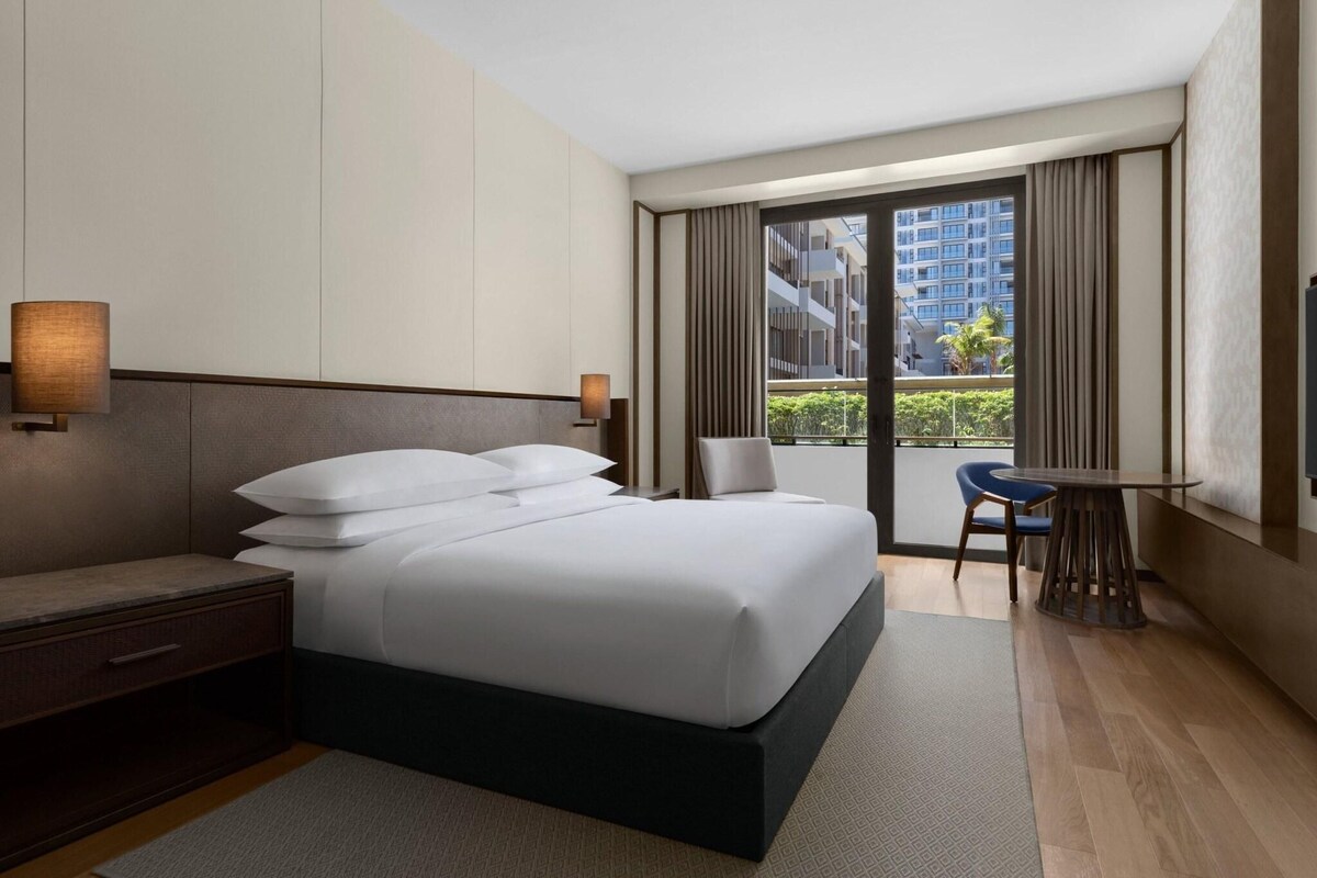 A modern hotel room with a large bed, a desk, and a view of the city.