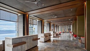 Eine geräumige Lobby mit einer langen Rezeption, einer Sitzecke und großen Fenstern mit Blick auf das Meer.