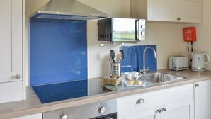 A modern kitchen with a blue backsplash, stainless steel appliances, a microwave, a toaster, and a kettle. - Pheasant Lodge at Wood House (Consett)
