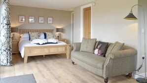 A bedroom with a wooden bed, a grey sofa, and a bedside table with a lamp. - Pheasant Lodge at Wood House (Consett)