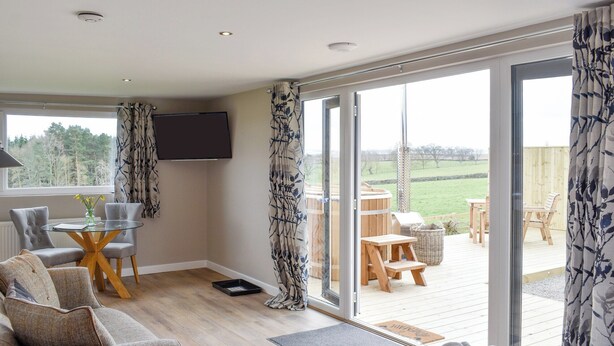 A modern living room with a glass door leading to an outdoor deck. - Pheasant Lodge at Wood House (Consett)