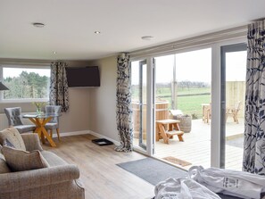 A modern living room with a glass door leading to an outdoor deck. - Pheasant Lodge at Wood House (Consett)