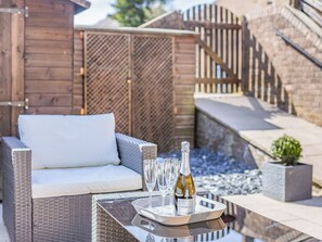A wicker sofa with a white cushion, a tray with glasses and a bottle of Prosecco, and a stone wall in the background. - Situated in the old part of Alnwick town centre sits Hotspur View. (Alnwick)