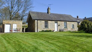 A stone house with a sloped roof, a chimney, and a small garden area with a bench and a table.