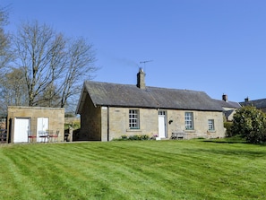 A stone house with a sloped roof, a chimney, and a small garden area with a bench and a table.