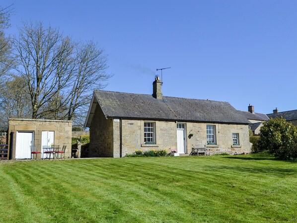 A stone house with a sloped roof, a chimney, and a small garden area with a bench and a table.