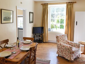 A dining area with a wooden table set for four, a television on a stand, and a floral armchair.