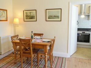 A dining area with a wooden table set for four, flanked by chairs, a lamp, and framed pictures on the wall. - Keepers Cottage Burradon (Burradon near Thropton)