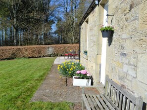 A stone building with a bench and flower pots. - Keepers Cottage Burradon (Burradon near Thropton)