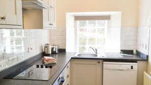 A kitchen with white cabinets, a black countertop, a Bosch dishwasher, a window with a view, and a sink.