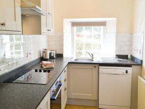 A kitchen with white cabinets, a black countertop, a Bosch dishwasher, a window with a view, and a sink. - Keepers Cottage Burradon (Burradon near Thropton)