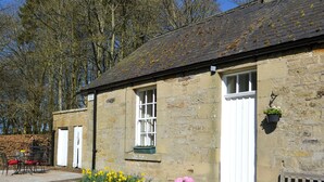 A stone building with a white door, a window with a green frame, and a bench outside.