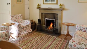 A cozy living room with a fireplace, floral-patterned sofas, and a striped rug.