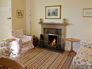A cozy living room with a fireplace, floral-patterned sofas, and a striped rug. - Keepers Cottage Burradon (Burradon near Thropton)