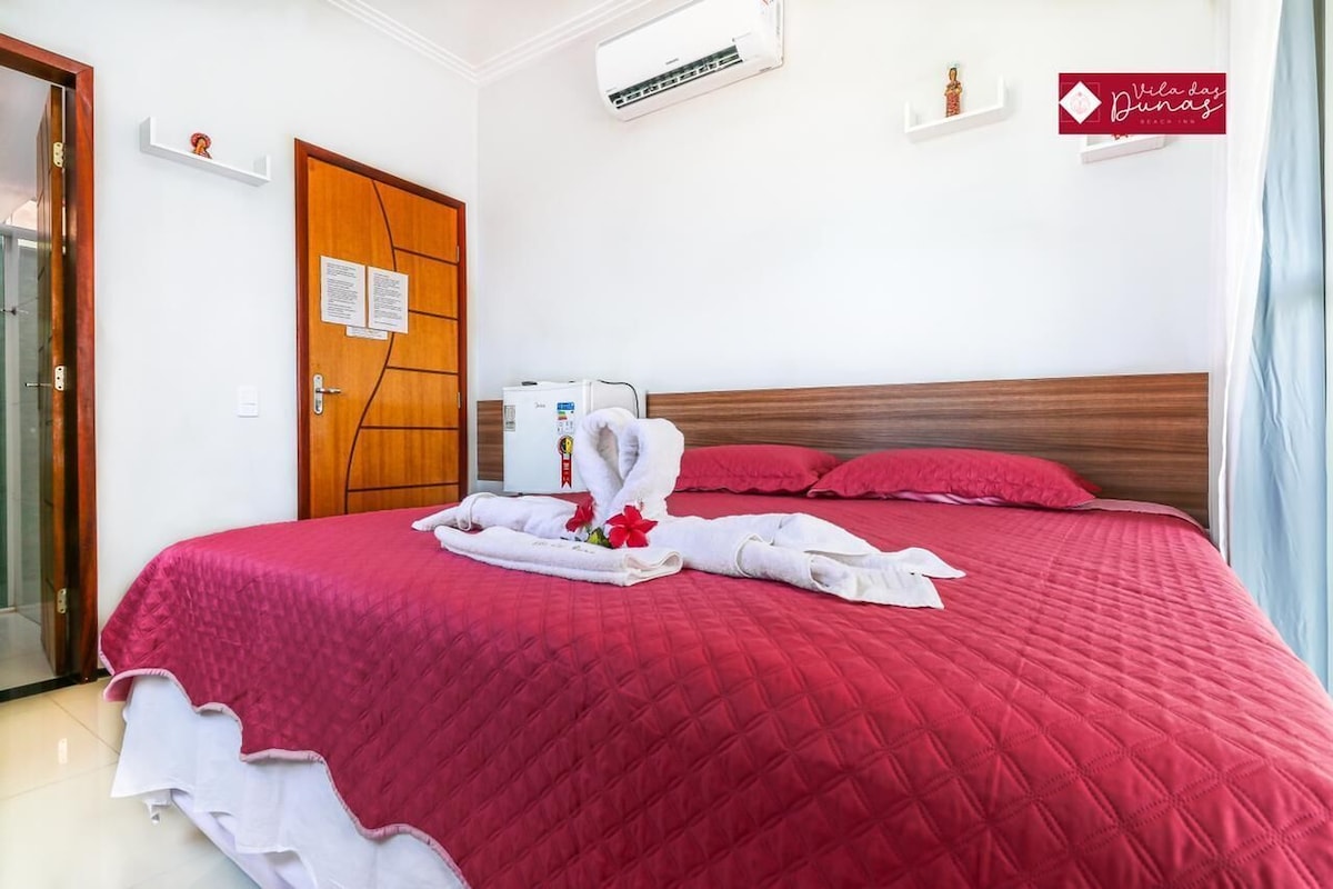 Ein Hotelzimmer mit rotem Überwurf, einer Holztür, einer Klimaanlage und einem Schild an der Wand.