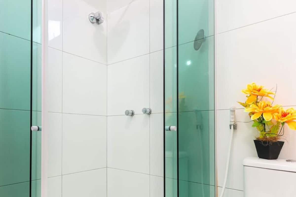 A shower with glass doors and a potted plant with yellow flowers on a white surface.