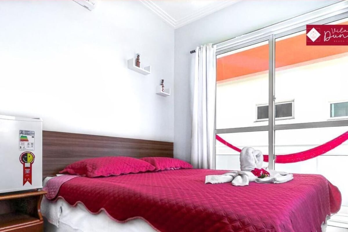 Ein Hotelzimmer mit einem Bett, einem Nachttisch, einem Fenster mit Vorhängen und Blick auf ein Gebäude.
