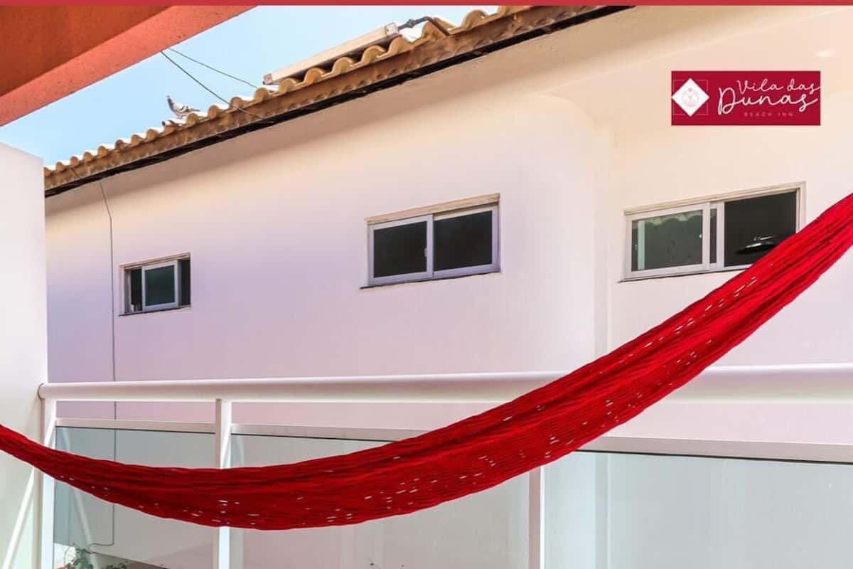 A building with a red fabric draped over a balcony railing, a tiled roof, and multiple windows.