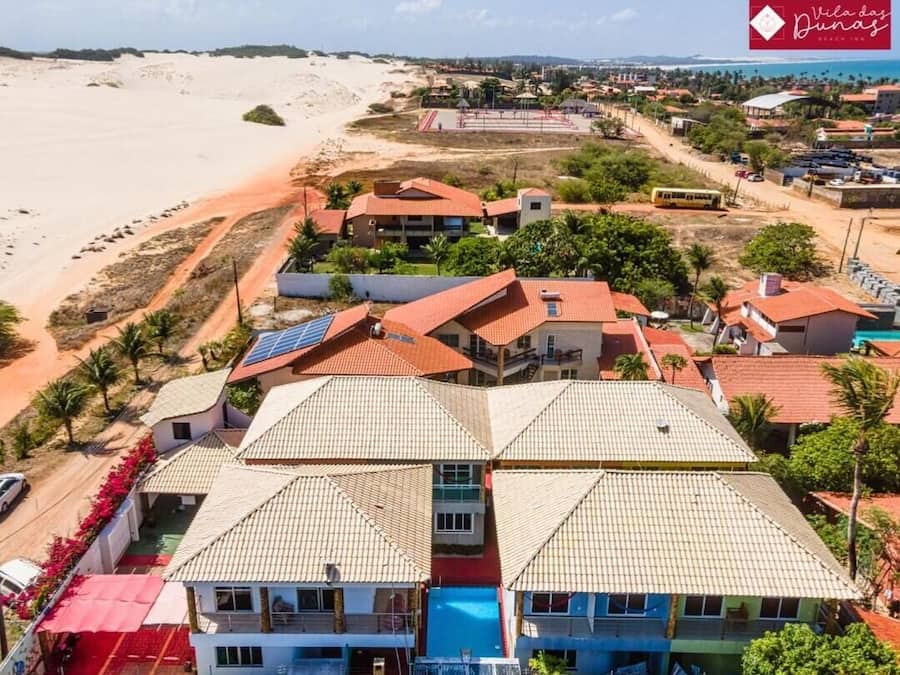 Zona residencial costera con casas de techo rojo, algunas con paneles solares, y una playa al fondo.