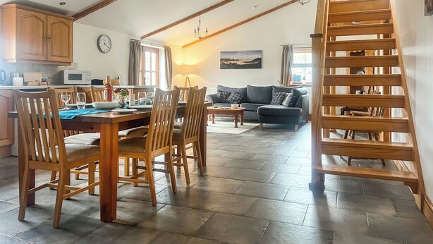 Un vaste espace de vie comprenant une table à manger, des chaises en bois, un canapé et un escalier en bois.